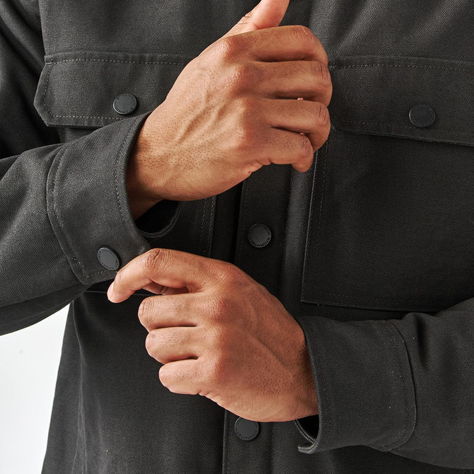 A men's dark grey oxford canvas jacket with a sherpa lining and snap-button closures on the cuffs and chest pockets.
