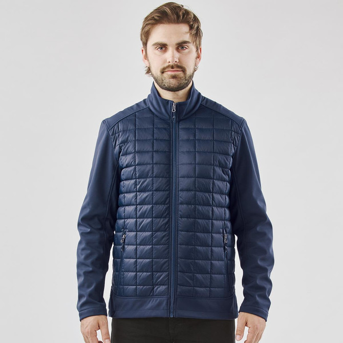 A men's softshell jacket in navy blue featuring a quilted front and zippered pockets. The jacket includes a logo.