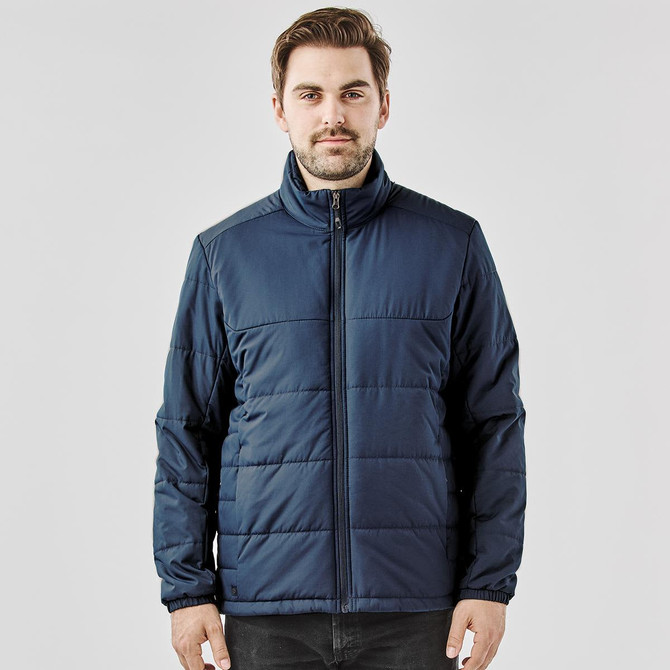 A man wearing a navy blue puffer jacket with a zippered front and a high collar. The jacket has a branded logo.