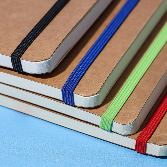 A stack of Jodha Notebooks in various colours: black, blue, green, and red, each with an elastic band.