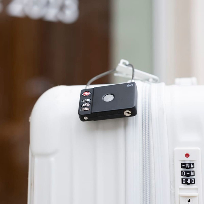 A black luggage lock is attached to a white suitcase, featuring a circular button and combination dials.