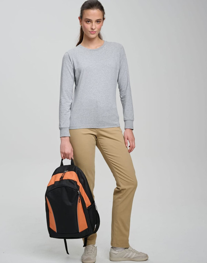 A young woman stands with an orange and black backpack, wearing a grey long-sleeve top and beige trousers.