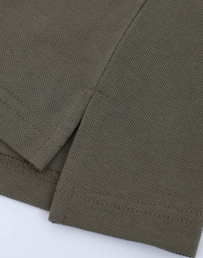 A close-up of olive green fabric with a textured surface, featuring the hem and sleeve of a polo shirt.