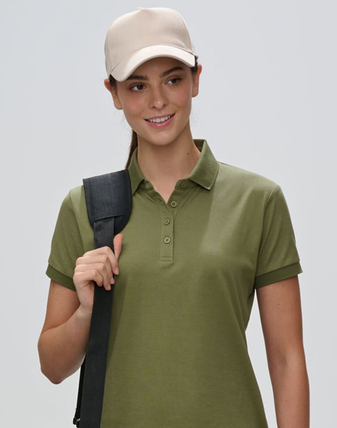 A woman wearing a khaki polo shirt and a beige cap, holding a black strap over her shoulder. The cap has a logo.