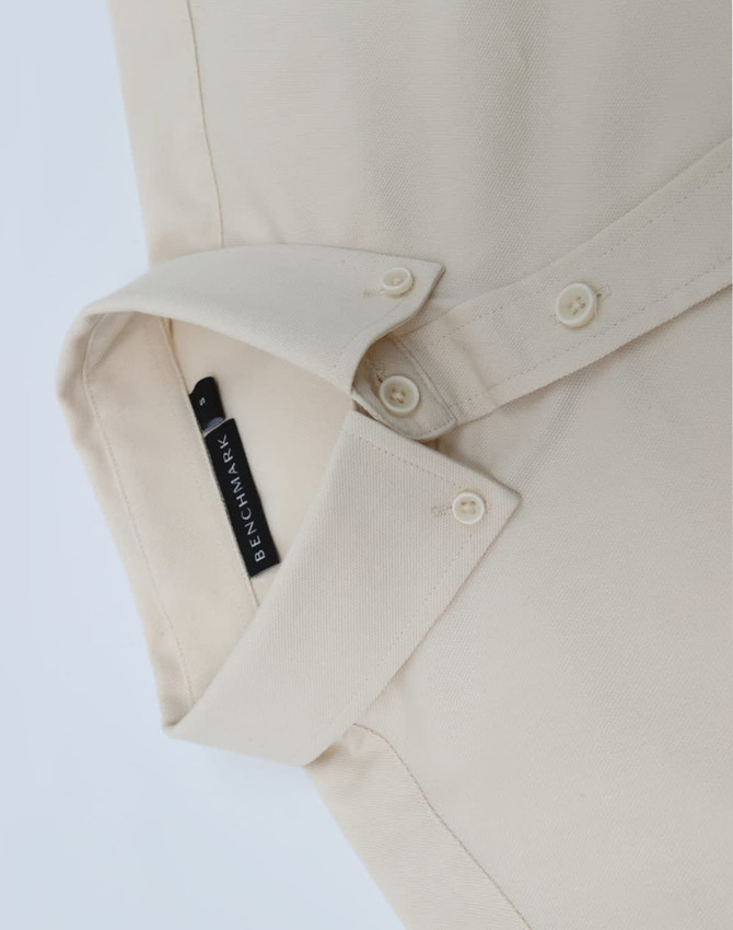 A beige men's long-sleeve shirt featuring a collar and buttons, with a branding label on the inside.