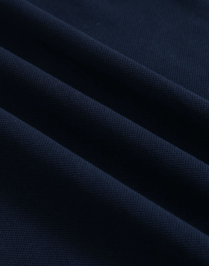 A close-up of navy ultrafine cotton pique fabric with textured folds. It features a subtle branding logo.