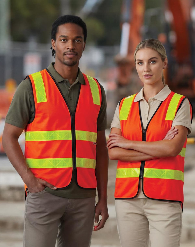 A high-visibility safety vest in bright orange with reflective strips, worn by two individuals on a construction site.