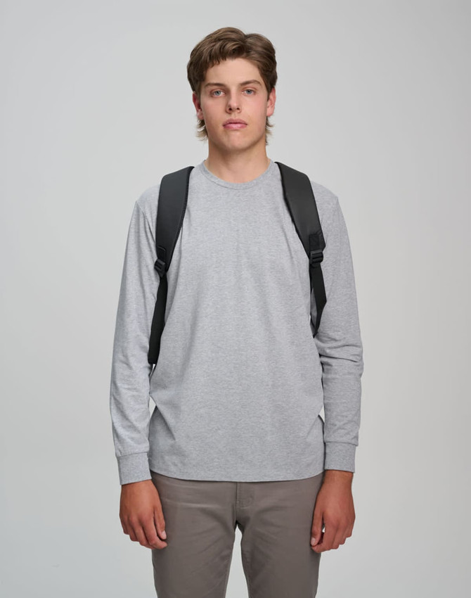 A model wearing a grey long-sleeve shirt and khaki pants, showcasing a black backpack on both shoulders.