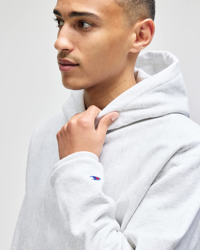 A light grey pullover hooded sweatshirt featuring a logo, worn by a young man with short hair.