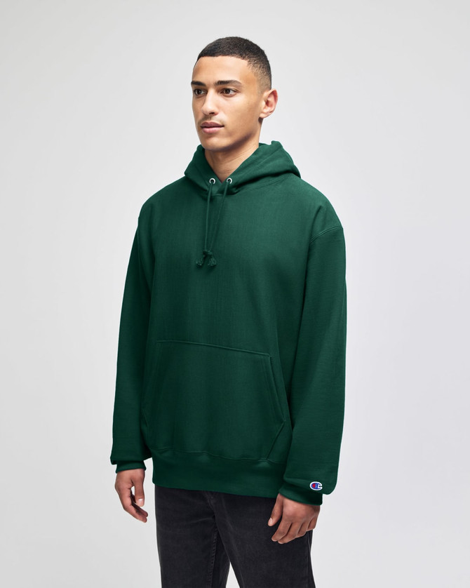 A green hooded sweatshirt with a front pocket and a logo on the sleeve, worn by a model.