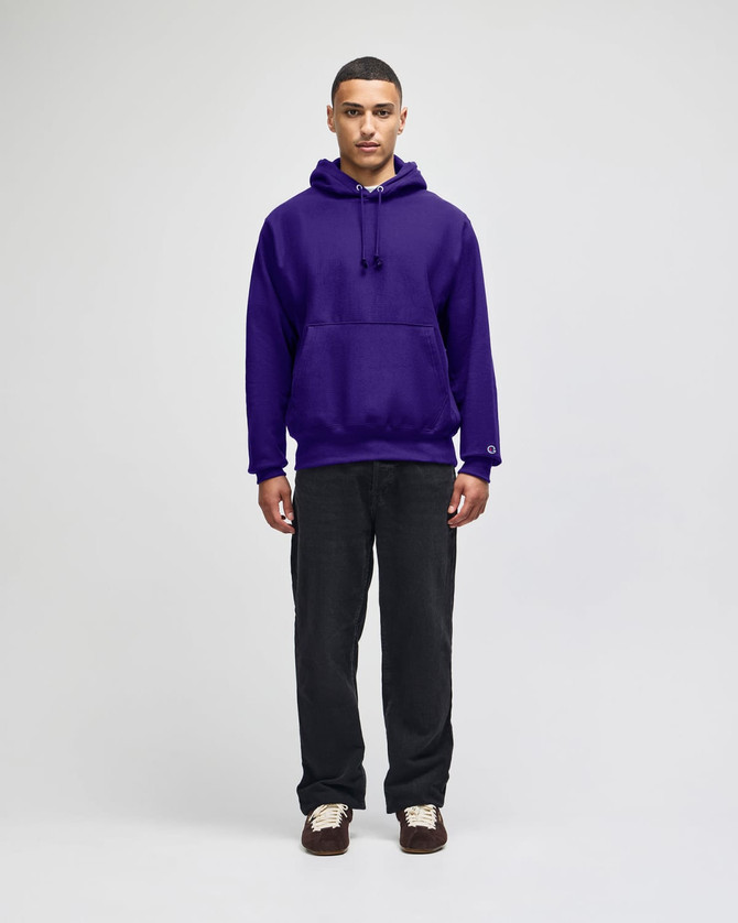 A purple pullover hooded sweatshirt with a front pocket and a logo, paired with dark pants.