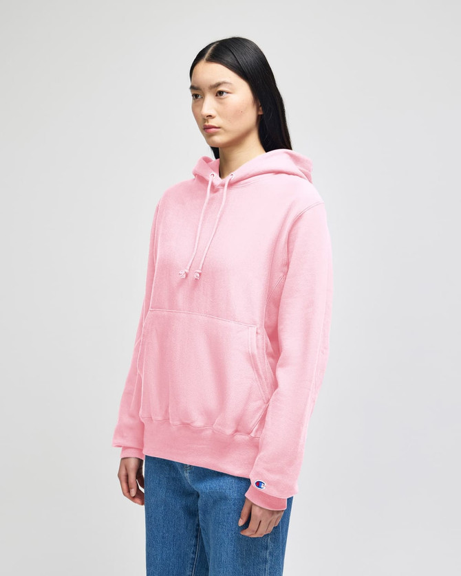 A pink Champion Reverse Weave® adult pullover hooded sweatshirt with a front pocket, worn by a model.