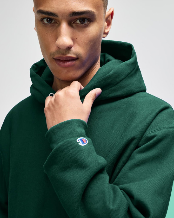 A green hooded sweatshirt with a logo on the sleeve, featuring a model showcasing its style and fit.
