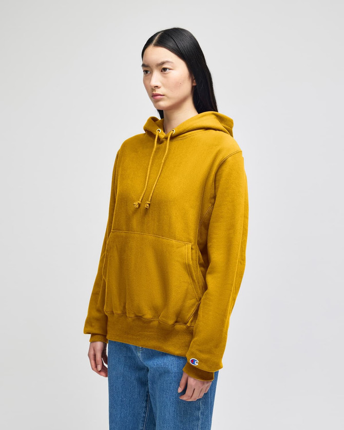 A mustard yellow pullover hooded sweatshirt with a front pocket and a logo on the sleeve.