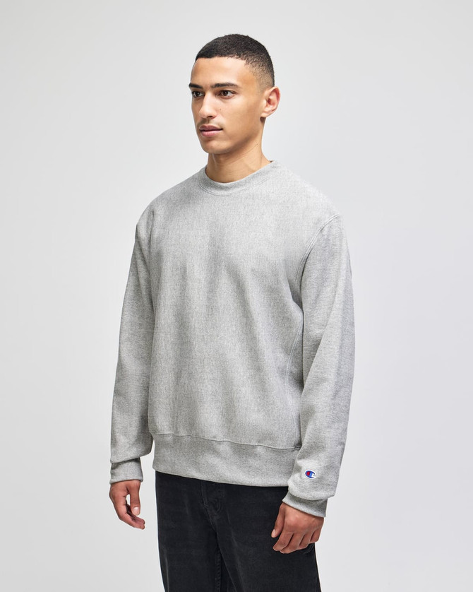 A grey Champion Reverse Weave® adult crew sweatshirt with a logo, modelled by a person.