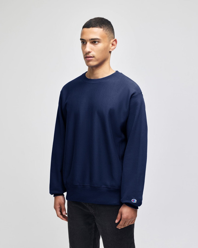 A navy blue Champion Reverse Weave® adult crew sweatshirt with a logo on the cuff, displayed on a model.