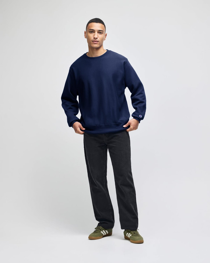 A navy blue sweatshirt with a crew neck and long sleeves, styled with dark pants and green shoes. The sweatshirt features a logo.