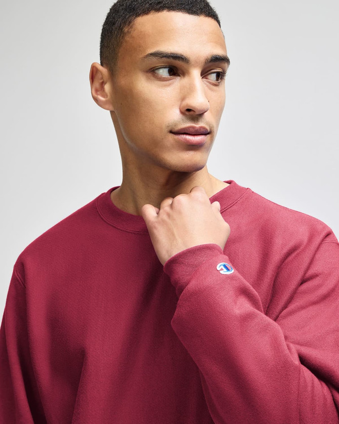A maroon Champion Reverse Weave® adult crew sweatshirt with a logo on the sleeve, featured on a model.