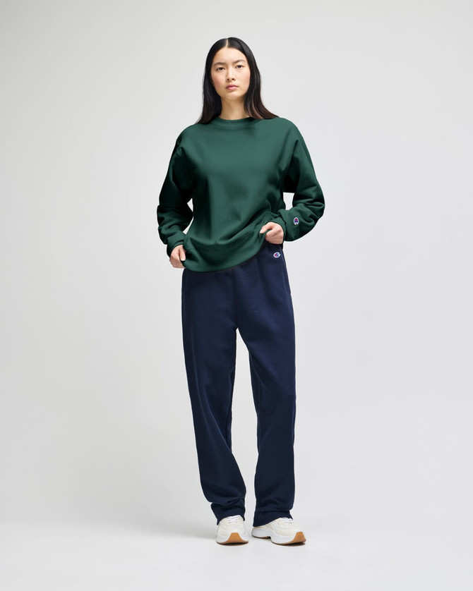 A green sweatshirt paired with navy trousers, featuring a logo on the sweatshirt. The model stands against a light background.