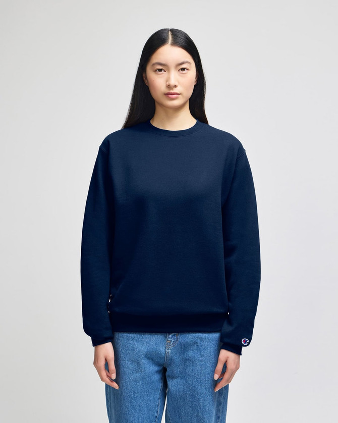 A navy blue crewneck sweatshirt is worn by a model, featuring a small logo on the sleeve.