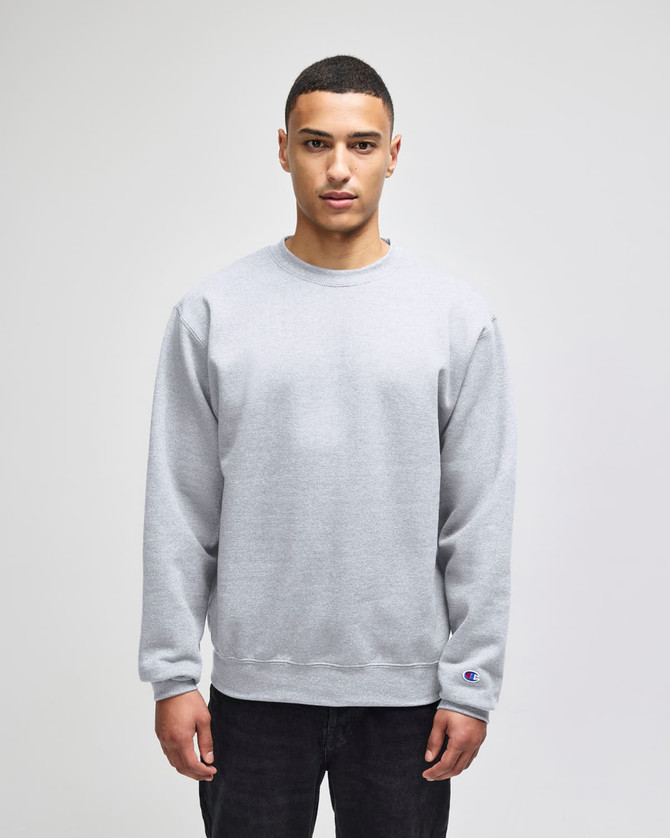 A grey Champion Powerblend® adult crewneck sweatshirt with a logo, featured on a model in casual attire.