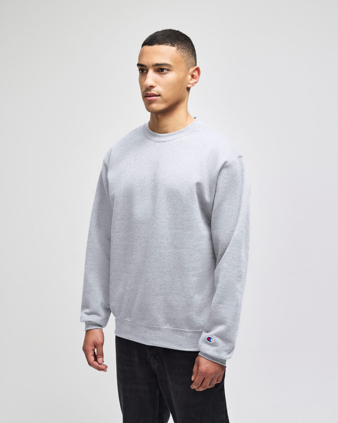 A grey adult crewneck sweatshirt on a model, featuring long sleeves and a logo on the sleeve.