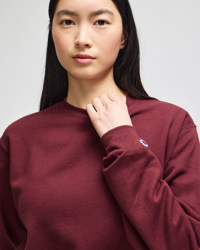 A maroon adult crewneck sweatshirt with a logo on the sleeve, featuring a relaxed fit design.