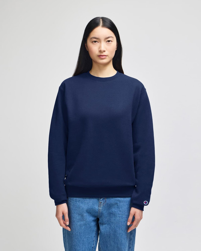 A navy adult crewneck sweatshirt is worn by a model, featuring a logo on the sleeve. The model pairs it with denim jeans.