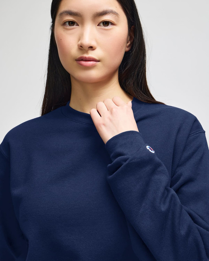 A woman wearing a navy blue sweatshirt with a small logo on the sleeve.
