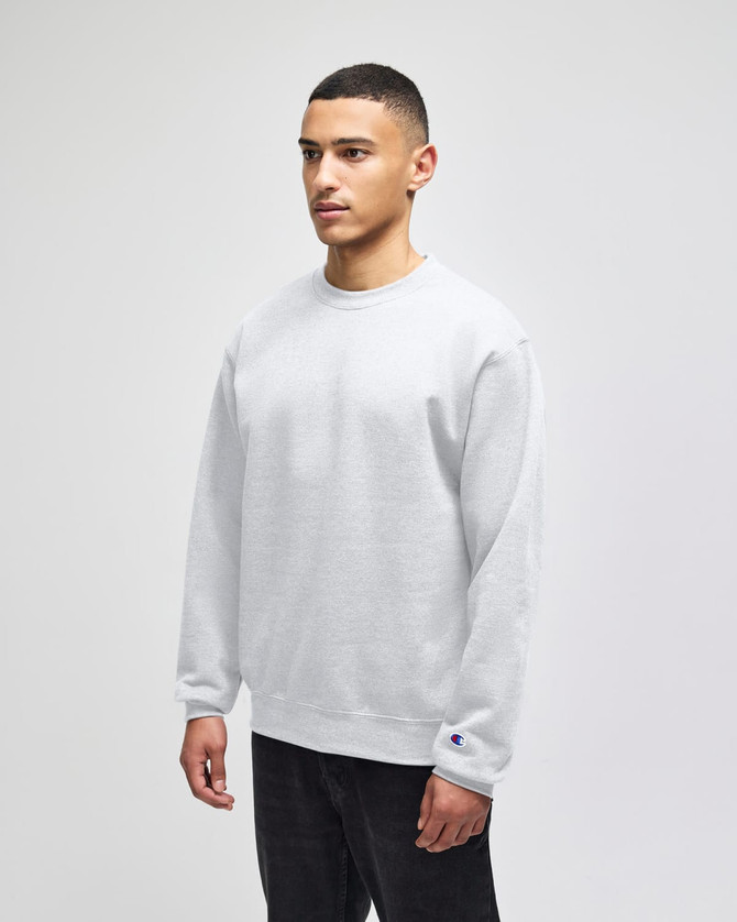 A grey crewneck sweatshirt on a model, featuring a small logo on the cuff.