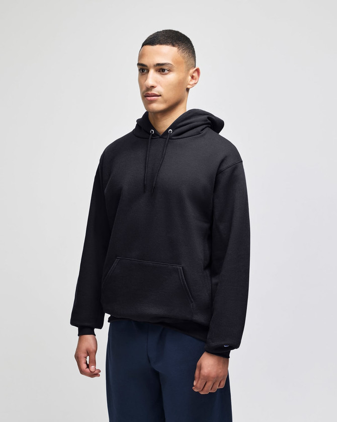 A black hooded sweatshirt with a front pocket and a hood, worn by a model. There is a logo on the garment.