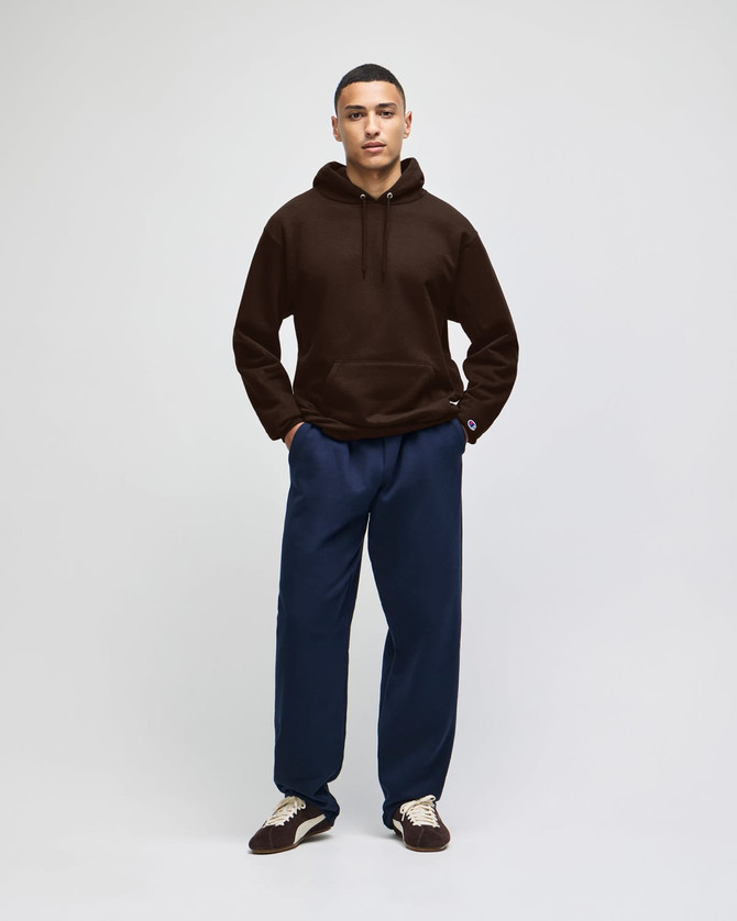 A brown hooded sweatshirt with a relaxed fit, paired with navy trousers and sneakers, featuring a logo.
