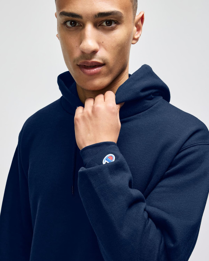A navy blue hooded sweatshirt with a logo on the sleeve, featuring a model wearing it.