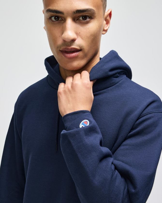 A model wearing a navy blue pullover hooded sweatshirt featuring a logo on the sleeve.