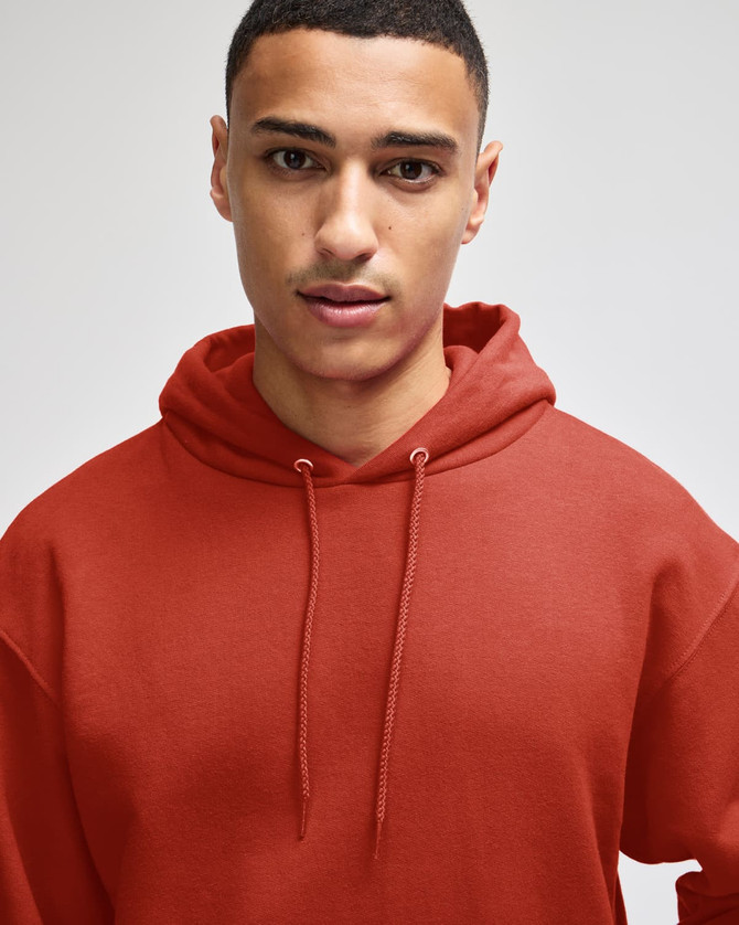A hooded sweatshirt in a rusty red colour, featuring a relaxed fit and a drawstring hood. It has a logo on the front.