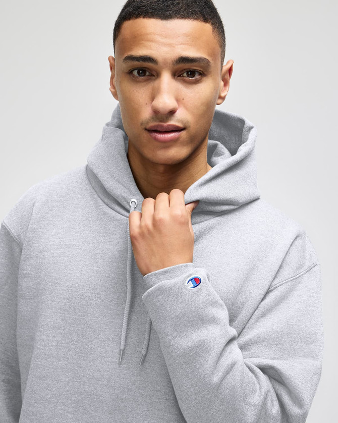 A grey hooded sweatshirt featuring a logo, with a male model wearing it and holding the hood.