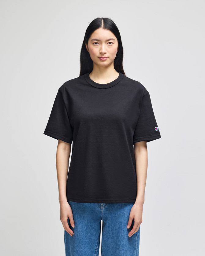 A black Champion Adult Heritage Jersey T-Shirt displayed on a model, featuring a logo on the sleeve.