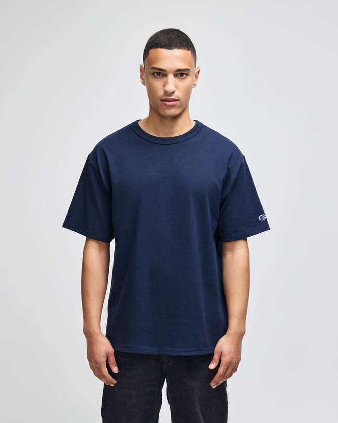 A navy blue Champion Adult Heritage Jersey T-Shirt on a model, featuring a logo on the sleeve.