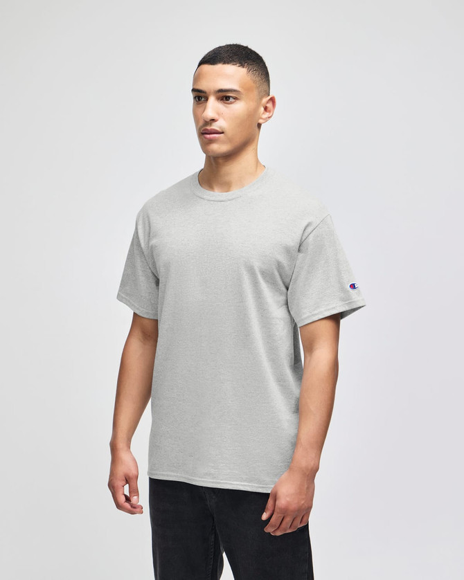 A grey Champion adult short-sleeve T-shirt displayed on a model. The shirt features a logo on one sleeve.