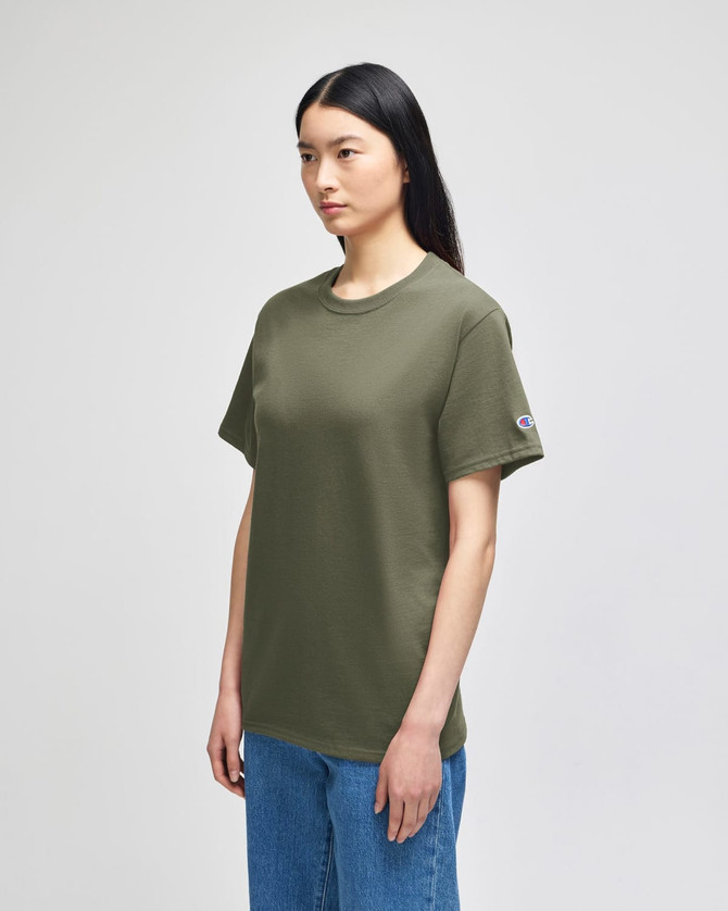 An olive green short-sleeve t-shirt displayed on a model with straight black hair, featuring a logo on the sleeve.