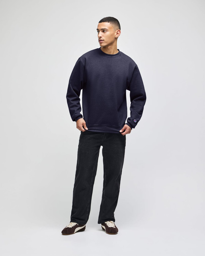 A model in a navy short-sleeve t-shirt paired with black trousers and brown shoes, featuring a logo on the sleeve.