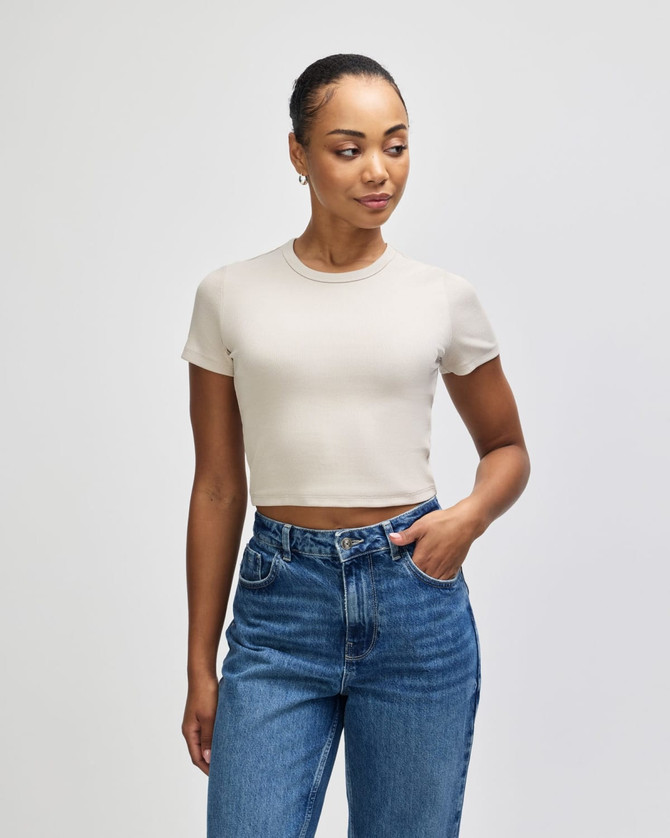 A fitted women's crop t-shirt in beige, paired with high-waisted blue jeans. The shirt has a logo.