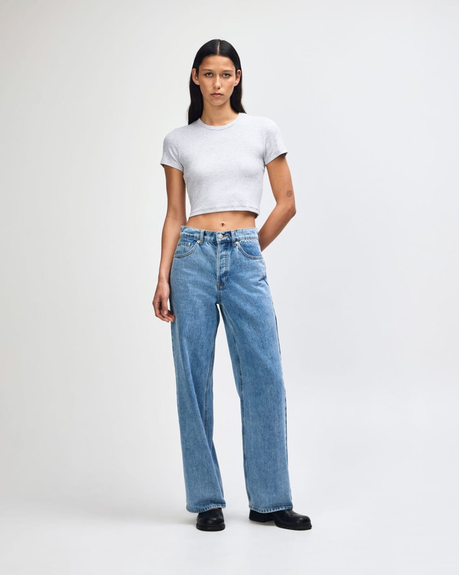A fitted grey crop t-shirt paired with high-waisted blue jeans. The model stands confidently against a neutral background.