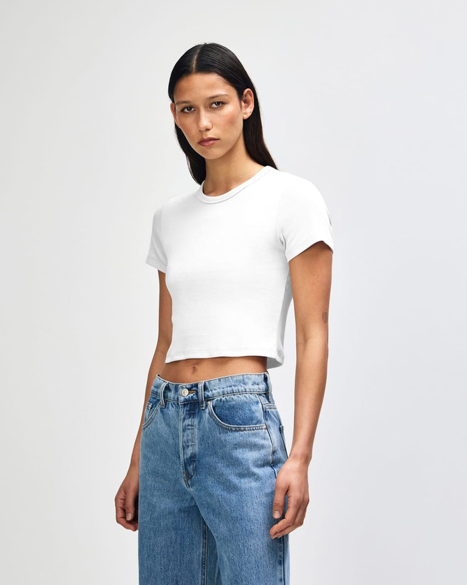 A white cropped fitted T-shirt on a model, paired with light blue jeans, featuring a logo.