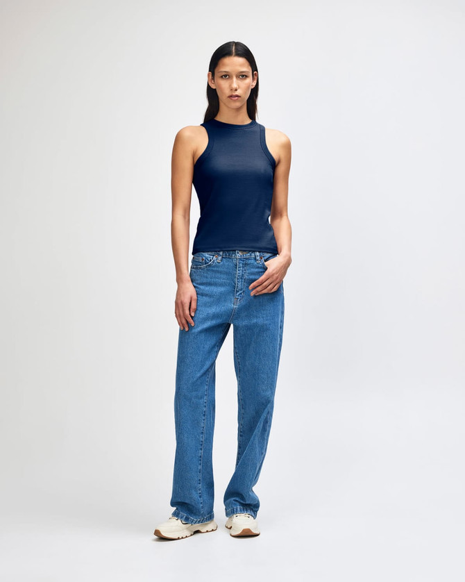 A fitted tank top in navy blue, paired with blue jeans, modelled by a woman standing against a plain background.