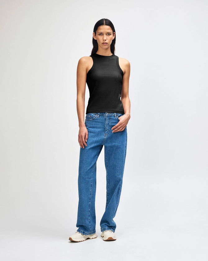 A fitted black tank top displayed on a model, paired with blue jeans and white shoes. The top features a logo.