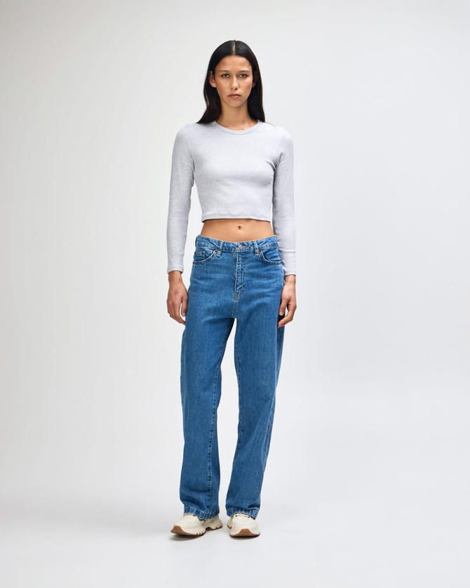A fitted grey long sleeve crop top paired with loose blue jeans, modelled by a standing woman.
