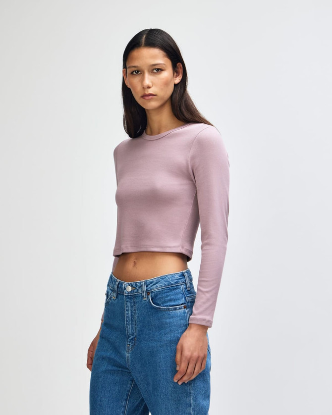 A fitted long-sleeve crop T-shirt in a soft lavender colour, worn by a model with straight hair, paired with blue jeans.
