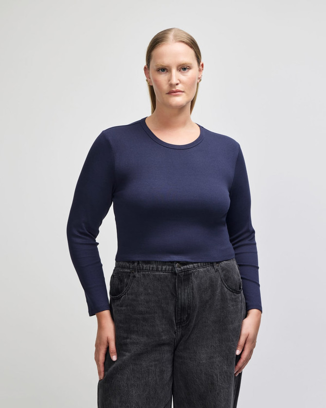 A fitted women's long sleeve crop t-shirt in navy blue, paired with high-waisted black pants. The shirt has a logo.