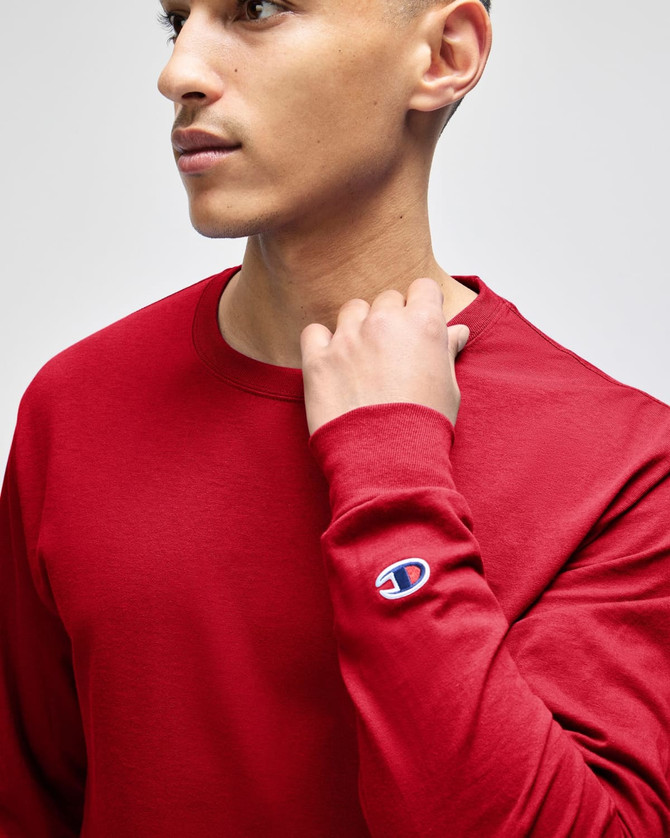 A long-sleeve t-shirt in red, featuring a small logo on the sleeve, worn by a model.